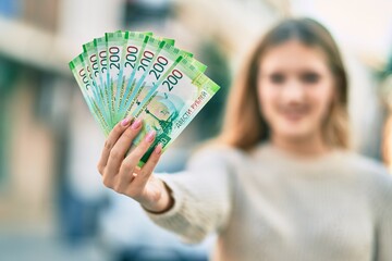 Beautiful caucasian teenager smiling happy holding russian 200 ruble banknotes at the city.
