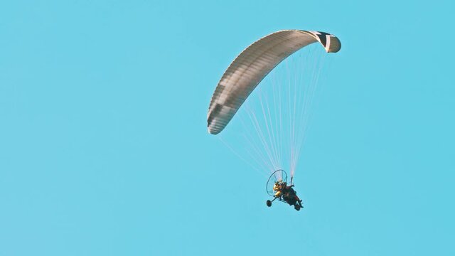 Low angle view of flying paramotor in air. Parachute against blue sky. Tandem motor powered paragliding at twilight. 