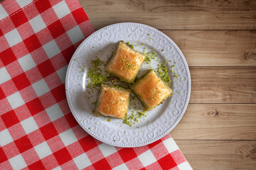 Plate, red cover and baklava with pistachio on the wooden table.