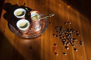 Traditional, oriental coffee cooked in turkish copper coffee pot poured in a cup. Oriental plate, pot and coffee cup. Coffe beans on table.