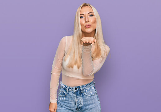 Young blonde woman wearing casual clothes looking at the camera blowing a kiss with hand on air being lovely and sexy. love expression.