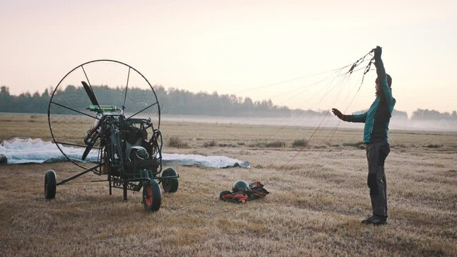 Pilot checking parachute cords. Pre-flight procedure. Tandem motor powered paragliding at twilight. 