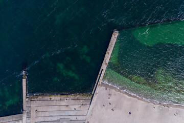 Sandy beach, concrete pier, clear sea water. Helicopter view.