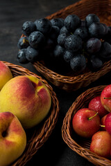 Some plums, peaches and grapes in some baskets on a black table with a black background