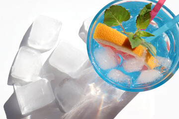 Summer cocktail with grapefruit and mint on white background. Refreshing drink with ice cubes. Glass of lemonade with citrus fruit. Hard light, shadow. Top view, copy space