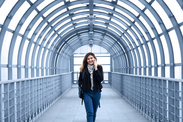 young woman laughing while talking on the phone walking on the covered overpass