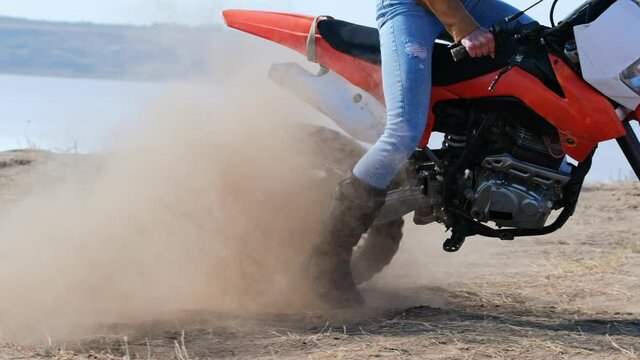 Slow motion video, the rear wheel of a motocross sport bike spins in place and kicks up dust.