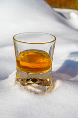 Glass of cold scotch single malt whisky on white snow