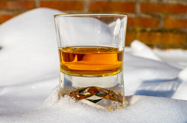 Glass of cold scotch single malt whisky on white snow