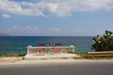 Obraz premium two empty red chairs and a table by the sea on Crete island (Greece)