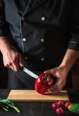 A professional chef is cutting red peppers for salad on a restaurant kitchen table. Vegetable diet or snack idea