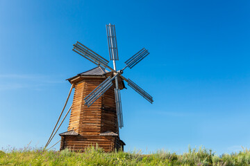 An old ruined wooden mill at the top of a blooming meadow against a bright blue sky.
