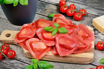 Red heart ravioli with tomato, mozzarella and basil on a wood background