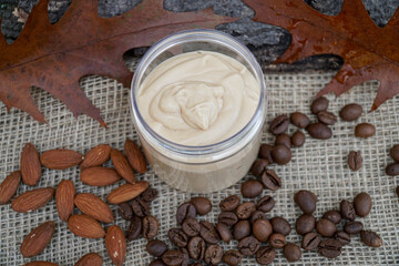           Natural handmade coffee and almond body butter with coffee beans and almond oil on beige and wooden background. Coffee and almond face cream, natural skin care.     