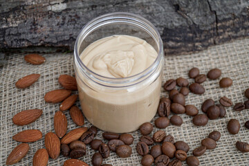           Natural handmade coffee and almond body butter with coffee beans and almond oil on beige and wooden background. Coffee and almond face cream, natural skin care.     