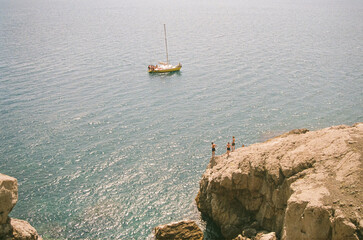 Tourists in the summer on the rocky beach. Yacht at sea.