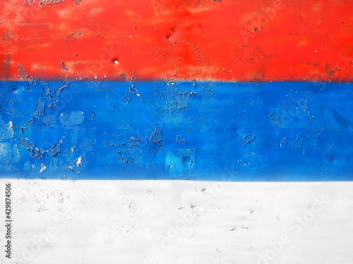 Serbian flag, tricolor red, blue, white painted on a metal surface. Peeling paint