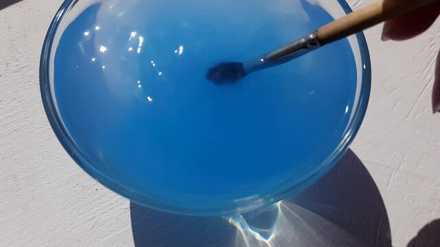 A wooden squirrel brush is rinsed from blue paint in transparent glass.