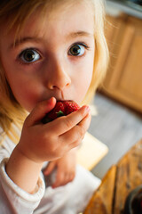 Little child girl eats fresh ripe strawberries in the morning at breakfast. Home garden, healthy food, child's diet. High quality photo
