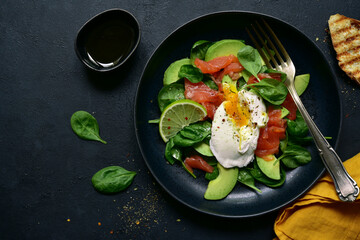 Fototapeta na wymiar Avocado and baby spinach salad with salted salmon and poached egg. Top view with copy space.