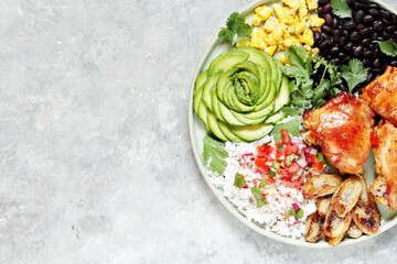 latin american food bowl - rose avocado, rice, salsa, fried banana, spiced baked chicken thighs, black beans, corn, cilantro.
top view. Copy space.