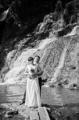 The bride and groom stand against the background of a waterfall. Newlyweds on the background of a waterfall