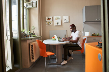 Male is sitting in cozy kitchen and using notebook