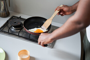 Man fries eggs at the pan while preparing breakfast for himself at the kitchen