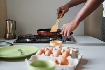 Man fries eggs at the pan while preparing breakfast for himself at the kitchen