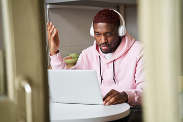 Man wearing headphones is browsing at his laptop and calling with customer