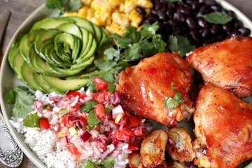 latin american food bowl - rose avocado, rice, salsa, fried banana, spiced baked chicken thighs, black beans, corn, cilantro.