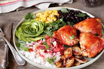 latin american food bowl - rose avocado, rice, salsa, fried banana, spiced baked chicken thighs, black beans, corn, cilantro.