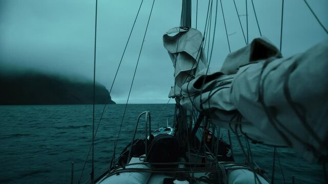 Yacht with lowered sails sails on the night ocean among the fog, swaying on the waves. 