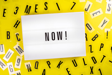 Lightbox with text NOW on yellow background with black letters randomly scattered. Concept of motivation, hurry up sale announcement, start, buy now, register, join, in stock, actual info trends