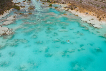 People swimming in sunny seven colored lagoon surrounded by tropical plants in Bacalar, Quintana Roo, Mexico