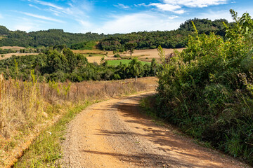 Fototapeta na wymiar Dirty road with farm fields, forest and mountains