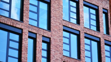 Modern brick and glass facade of the office building.  A contrasting combination of sky and brick texture on a building. Architectural facade of a red brick building..