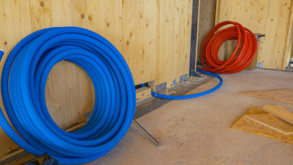CLOSE UP: Coil of blue rubber tubing is rolled out underneath the wooden wall.