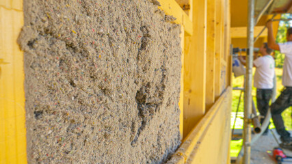 CLOSE UP: A group of workers blow cellulose insulation into the wooden walls. - obrazy, fototapety, plakaty