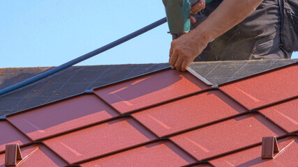 CLOSE UP: Unrecognizable roofer lays aluminium tiles with the help of a nail gun