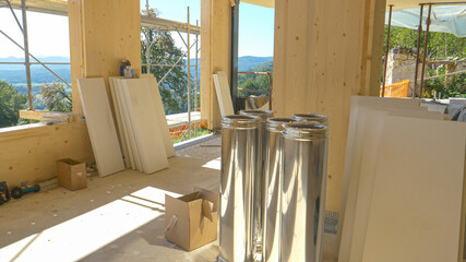 Shiny stainless steel chimney tubes lie on ground of a house under construction.