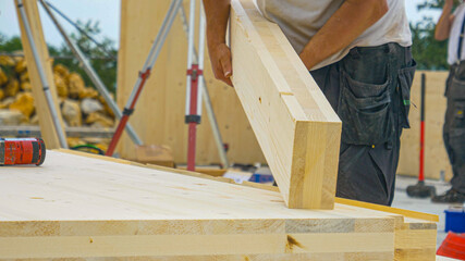 CLOSE UP: Unrecognizable male builder picks up a CLT beam from a workbench.