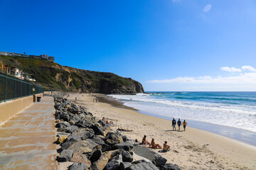people walking along the beach on silky sand near vast blue ocean water with waves rolling in and blue sky at Dana Strands Beach in Dana Point California USA - obrazy, fototapety, plakaty