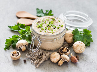 Vegan mushroom pate with green onions, parsley in a glass jar on a linen napkin on a light gray...