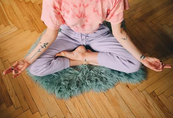 Tuinposter Woman meditating at home while sitting at the floor in lotus pose © Yakobchuk Olena