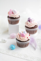Three Easter chocolate cupcakes with caramel filling and decoration of small Easter eggs from marzipan on the white background. Selective focus