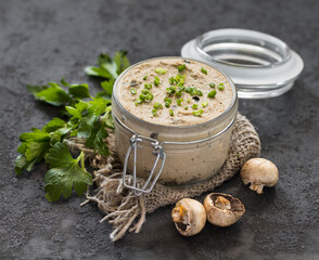 Champignon pate with green onions, parsley in a glass jar on a linen napkin on a dark gray background in rustic style