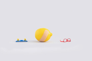 Creative concept with lemon with adhesive bandage, eyeglasses and skateboard on grey background