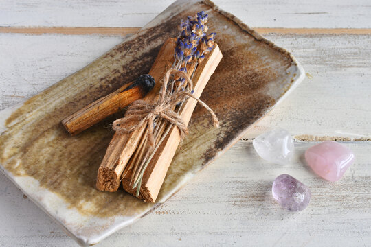 A close up image of wooden incense sticks with dried lavender and healing crystals on a white background. 