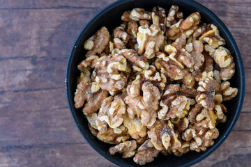 Toasted walnuts in a round black ceramic bowl on a wooden background
